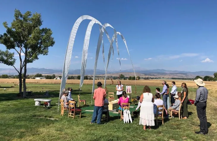 A graveside service in an open field, family gathered beneath tall white prayer flags