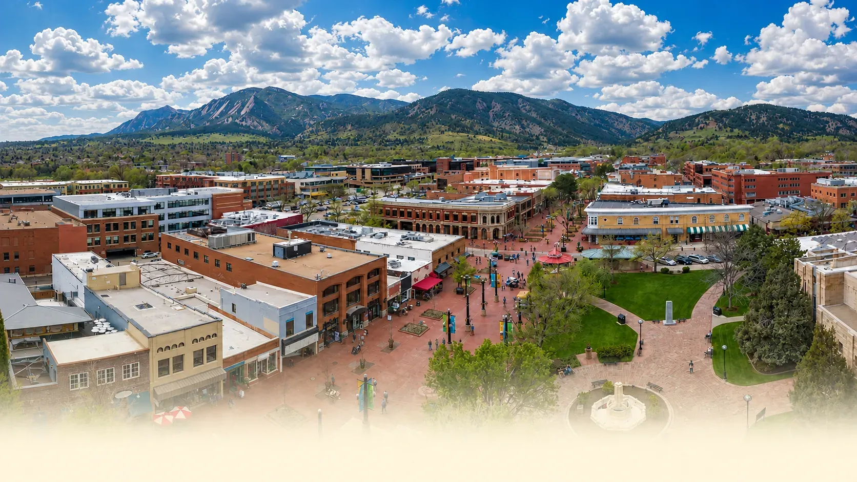 An aerial view of downtown Boulder's Pearl Street, with the Flatirons rising behind it